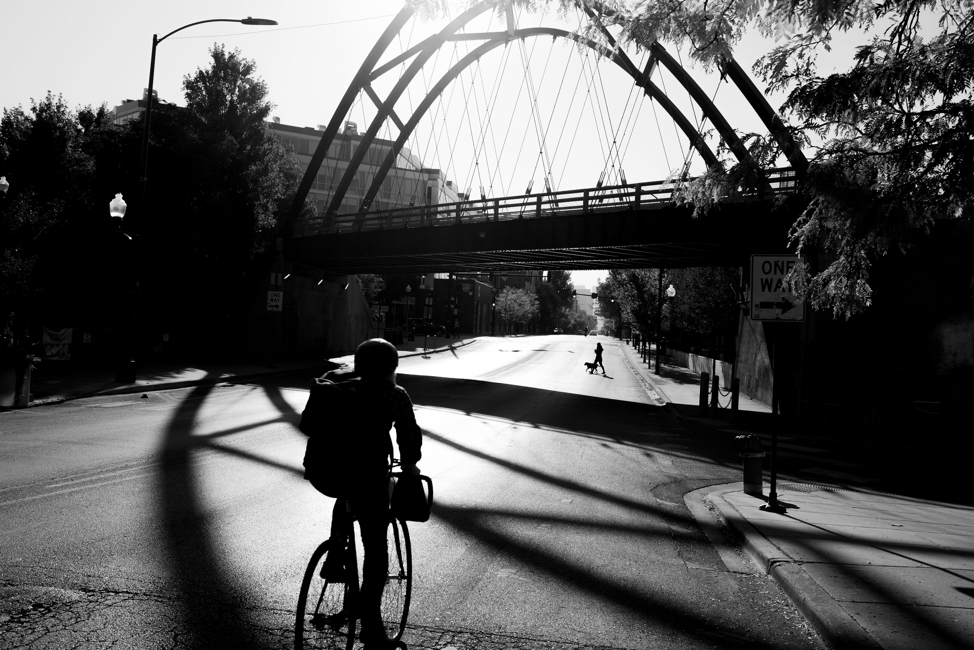 Black and white photo of a man riding a bike toward a bridge in the Bucktown neighborhood of Chicago